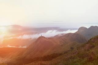 Einsamer Wanderer auf Berggipfel, umgeben von Wolken und Nebel.